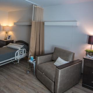 A cozy hospital patient room featuring a bed, seating area, and soft lighting.