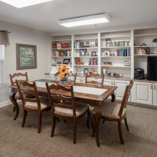 A cozy dining room with a wooden table and chairs, surrounded by bookshelves filled with various items.
