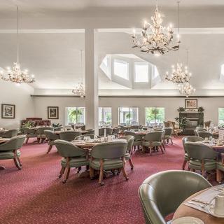 Spacious dining room with elegant chandeliers and large windows, featuring round tables and comfortable chairs.