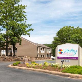 Exterior view of a building with a welcome sign and landscaped driveway.