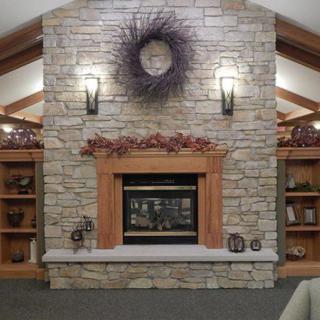 A cozy living room featuring a stone fireplace with wooden mantel and decorative elements, surrounded by built-in wooden shelves.