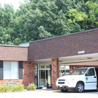 A brick commercial building with a van parked near the entrance, surrounded by trees.