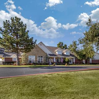 A suburban house surrounded by trees and a well-maintained lawn under a partly cloudy sky.