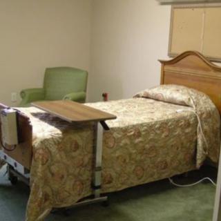 A simple hospital room with a bed, chair, and overbed table.