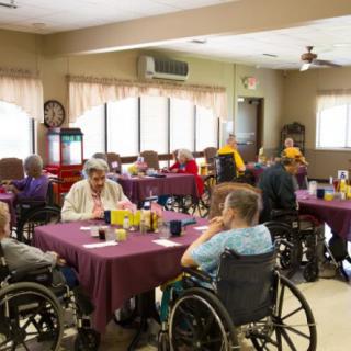 Seniors in wheelchairs gather in a nursing home's dining room for a meal and social interaction.
