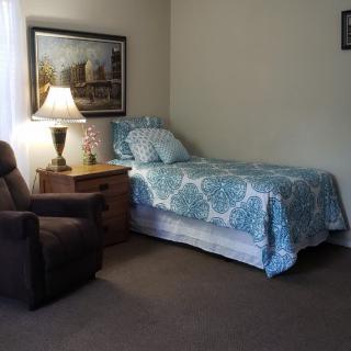 A cozy bedroom with a single bed, armchair, and nightstand.