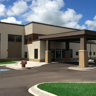 A modern commercial building with a covered entrance and a parking area under a partly cloudy sky.