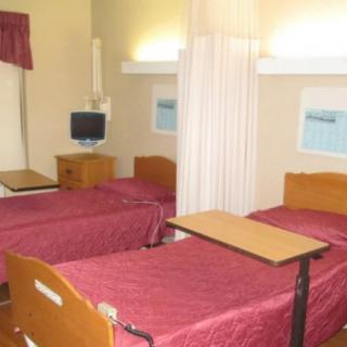 A hospital room with two beds, privacy curtains, and a small television.