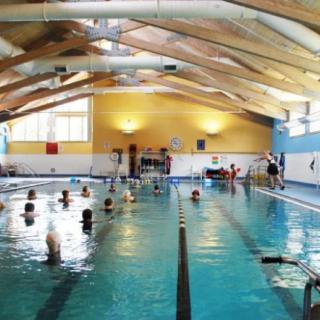 An indoor swimming pool with people participating in a swimming lesson.