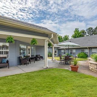 A cozy outdoor patio area in a residential setting, featuring garden furniture and umbrellas under a cloudy sky.