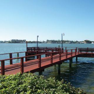 A wooden dock extends over a peaceful body of water under a clear blue sky.