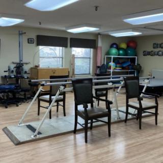 A rehabilitation room equipped with parallel bars, chairs, and fitness balls for physical therapy exercises.
