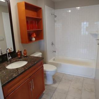 A modern bathroom with a granite countertop, wooden cabinets, and a clean white bathtub.