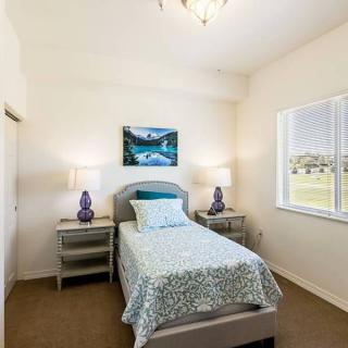 A cozy bedroom with a single bed, flanked by nightstands and lamps, featuring a window and wall art.