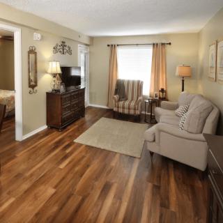 A cozy living room with wood flooring, featuring a comfortable sofa, chair, and a TV setup.