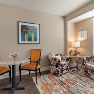A cozy living room with colorful chairs, a patterned rug, and artwork on the wall.