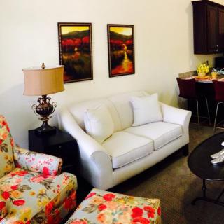 A cozy living room with a white sofa, floral armchairs, and a dining area in the background.