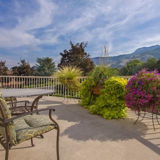 A peaceful patio with outdoor seating and lush garden plants offers a stunning mountain view under a clear blue sky.