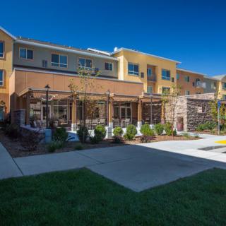 A modern residential apartment complex with well-maintained landscaping and outdoor pathways under a clear blue sky.