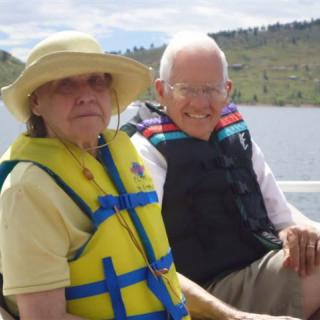 An elderly couple wearing life jackets enjoying a boat ride on a lake.