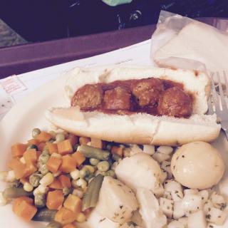 A meal featuring a bread roll with meatballs, accompanied by mixed and cauliflower vegetables.