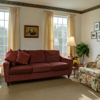 A cozy living room featuring a red sofa, floral armchair, and decorative elements like framed pictures and a potted plant.