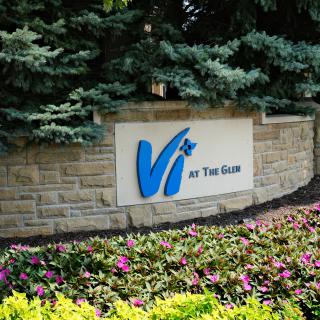 A stone sign surrounded by vibrant flowers and greenery at a building entrance.