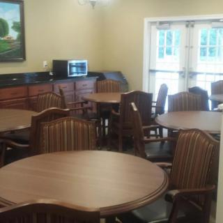 An empty dining area with several round tables and chairs, featuring a microwave and wall painting.
