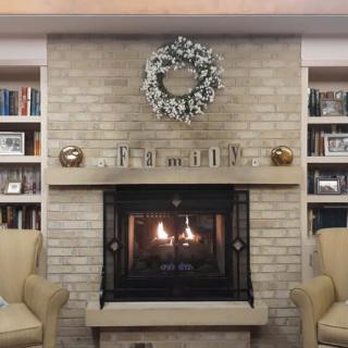 A cozy living room with a brick fireplace and wreath, flanked by bookshelves and comfortable chairs.