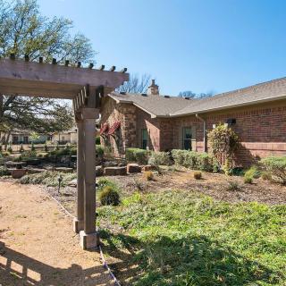 A beautifully landscaped garden with a wooden pergola and a brick building in the background on a sunny day.