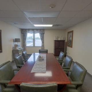 A conference room with a large meeting table and several chairs, featuring a window view and decorative elements.