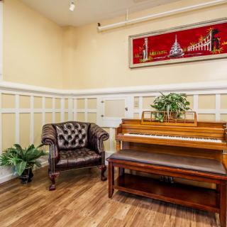 A cozy room with a wooden piano and leather armchair, featuring decorative plants and artwork.