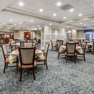 A well-lit dining area with neatly arranged tables and chairs on a patterned carpet.