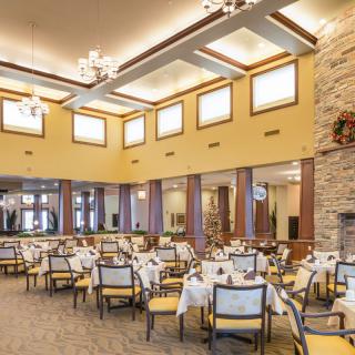A spacious indoor dining area with neatly arranged tables and chairs, illuminated by chandeliers.