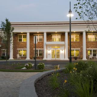 A colonial-style brick building with large columns, illuminated in the evening.