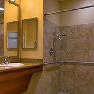 A well-lit bathroom featuring a mirror, sink, and tiled shower area.