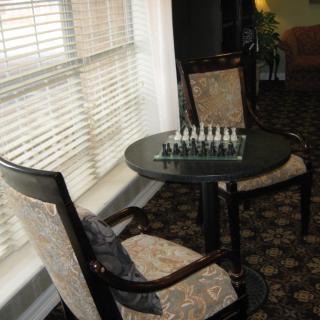 A cozy indoor seating area with a chess set on a small round table between two upholstered chairs by the window.