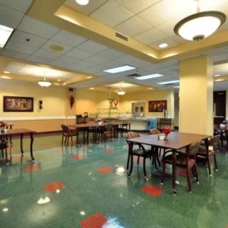An empty cafeteria with neatly arranged tables and chairs, lit by overhead lights.