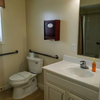 A bathroom with a toilet, sink, and mirror, featuring grab bars for accessibility.