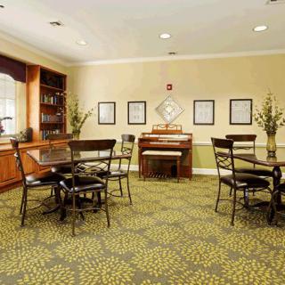 A cozy dining room with a patterned carpet, several tables and chairs, and a piano against the wall.