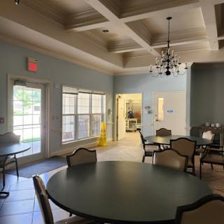 A bright and inviting community dining area featuring round tables and a chandelier under a coffered ceiling.