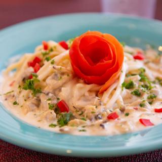 A plate of creamy pasta garnished with a carved tomato rose and diced vegetables.