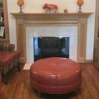 A cozy living room with a fireplace and a round ottoman.