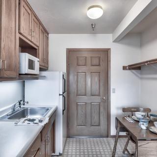 A compact kitchen with wooden cabinets, microwave, refrigerator, sink, and a small dining area.