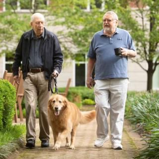 Two men walking a dog in a park.
