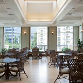 A spacious dining area with multiple tables and chairs, well-lit by natural light streaming through large windows.