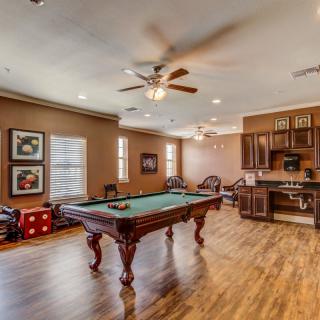 A cozy game room featuring a billiards table, complete with wood flooring and a kitchen area.