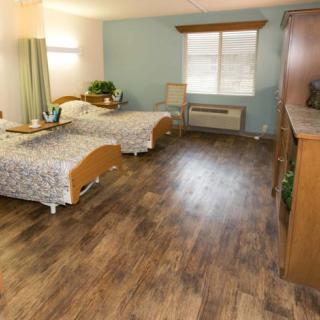 A spacious bedroom with twin beds and wooden flooring, illuminated by natural light from a window.