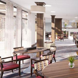 A modern lounge area featuring wooden furniture and ample natural light streaming through large windows.