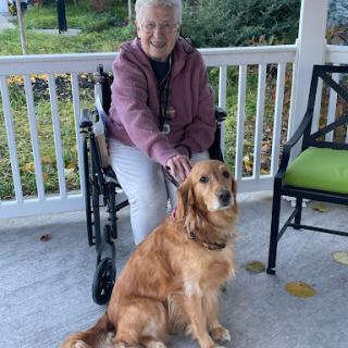 A senior woman sits on a porch with her golden retriever beside her, enjoying the outdoors.